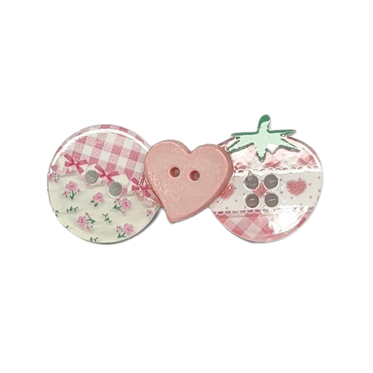 Three decorative buttons arranged side by side on a plain white background: a round button with pink gingham and floral print, a pink heart-shaped button with two holes, and a strawberry-shaped button with green leaves and a pink gingham pattern.